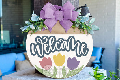 Digital SVG file for a round spring welcome door hanger featuring tulip flowers and script lettering. This instant download laser cut design allows you to create your own DIY porch sign using a Glowforge, xTool, or similar laser machine. Shown images are finished examples; this listing is for a digital file only, perfect for spring décor, floral door signs, and customizable round door hangers.