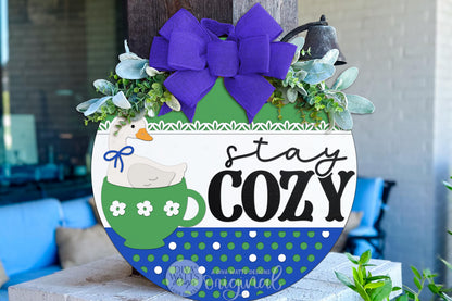 Digital SVG file of a round door hanger featuring a goose sitting inside a teacup with “stay cozy” text. This instant download laser cut design is ideal for cottagecore and grandma core DIY décor. The digital file allows you to create your own cozy porch or entryway sign using a laser machine, with layered elements designed for easy cutting, painting, and assembly.